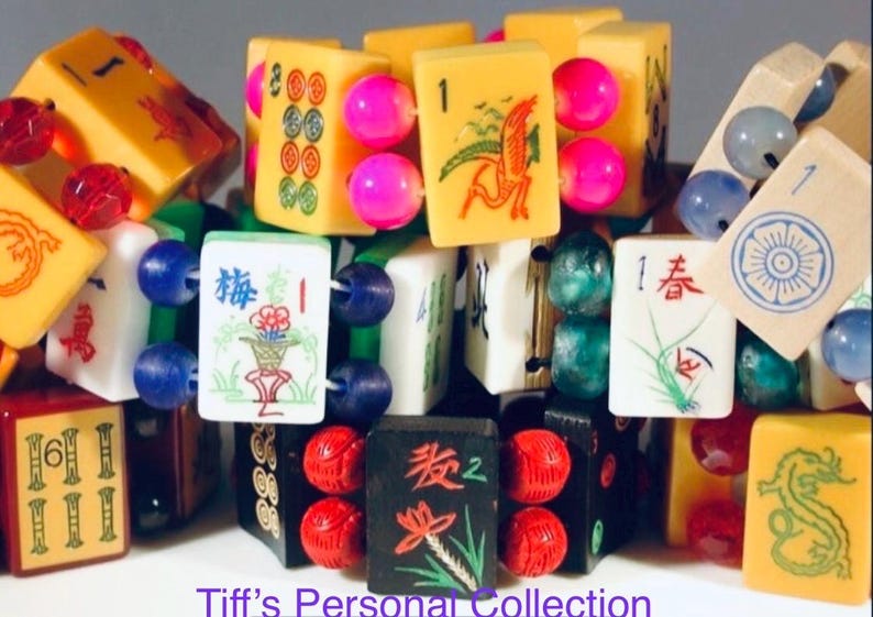 Puede incluir: Una colecci&oacute;n de pulseras hechas con fichas de mahjong vintage en varios colores, incluyendo amarillo, blanco y negro, con s&iacute;mbolos y caracteres grabados, conectadas por cuentas redondas de colores. El texto Tiff's Personal Collection es visible.