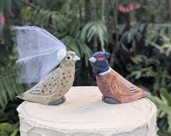 Topo de bolo de casamento com faisão-de-colar, pássaros de madeira esculpidos à mão representando noivos, decoração rústica para casamento no campo/jardim.