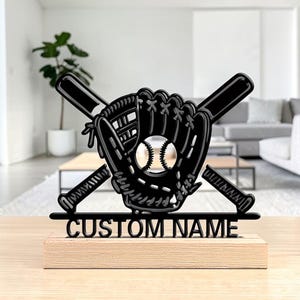 Könnte beinhalten: Schwarze Baseball-Dekoration mit Handschuh, Ball und gekreuzten Schlägern. Das Design enthält den Text "CUSTOM NAME" auf einem Holzsockel. Der Baseball ist silberfarben.
