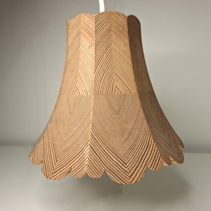 Puede incluir: Una lámpara colgante de madera con borde festoneado. La pantalla es de madera marrón claro con un patrón de espiga. La luz cuelga de un cable blanco.