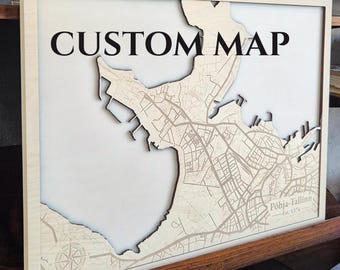 May include: A square wooden wall art piece featuring a laser-cut map of the Pohja-Tallinn area. The light-colored wood map is set against a white background within a thin wooden frame. The text CUSTOM MAP is printed at the top, with Pöhja-Tallinn Est. 1374 in the corner.
