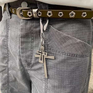 May include: A green belt with silver flower-shaped buckles and a silver cross charm hanging from it.