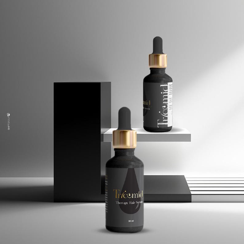 Może przedstawiać: Dwie czarne butelki serum do włos&oacute;w Tricemid Therapy ze złotymi zakraplaczami. Butelki stoją na białej p&oacute;łce i czarnym bloku. Etykieta zawiera nazwę marki i szczeg&oacute;ły produktu. Butelki mają po 30 ml.