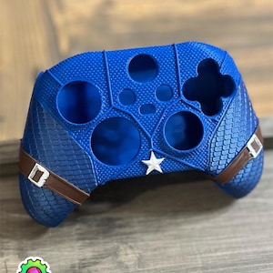 Op de afbeelding: Een blauwe 3D-geprinte Xbox-controller skin met een Captain America-ontwerp. De skin heeft een blauwe en witte ster en een bruine band.