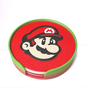 May include: Set of four red and green round coasters featuring a cartoon image of Mario from the Super Mario Bros. video game series.