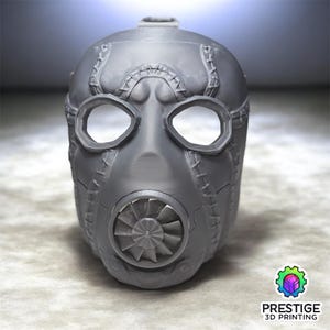 May include: A gray, stylized mask with large eye openings and a central respirator design. The mask features stitched detailing and a textured surface, suggesting a post-apocalyptic or industrial theme. The mask is a 3D printed item.