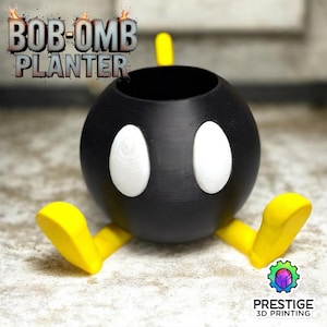 May include: A black Bob-Omb planter with white eye details and yellow feet. The planter has a round body and a circular opening at the top. The text "BOB-OMB PLANTER" is displayed at the top of the image.