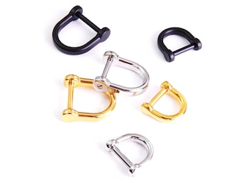 May include: An assortment of D-shaped shackles in various metallic finishes, including black, gold, and silver. The shackles are arranged on a white background, showcasing their design and construction. These hardware components are used for connecting ropes, chains, and other rigging.