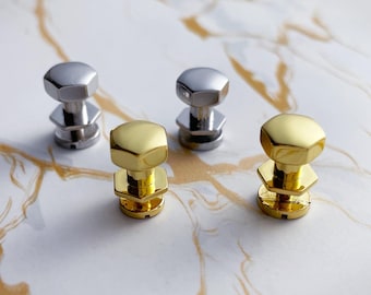 May include: Four metal decorative bolts, two silver and two gold, are arranged on a marble-patterned surface. Each bolt features a hexagonal head and a stacked base, showcasing a modern, industrial aesthetic. The bolts are designed for decorative purposes.
