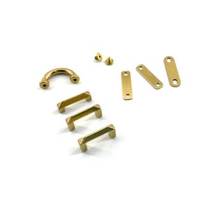 May include: A collection of brass hardware components, including curved handles, rectangular plates with holes, and screws. The hardware has a polished, golden finish, suitable for furniture or decorative projects.