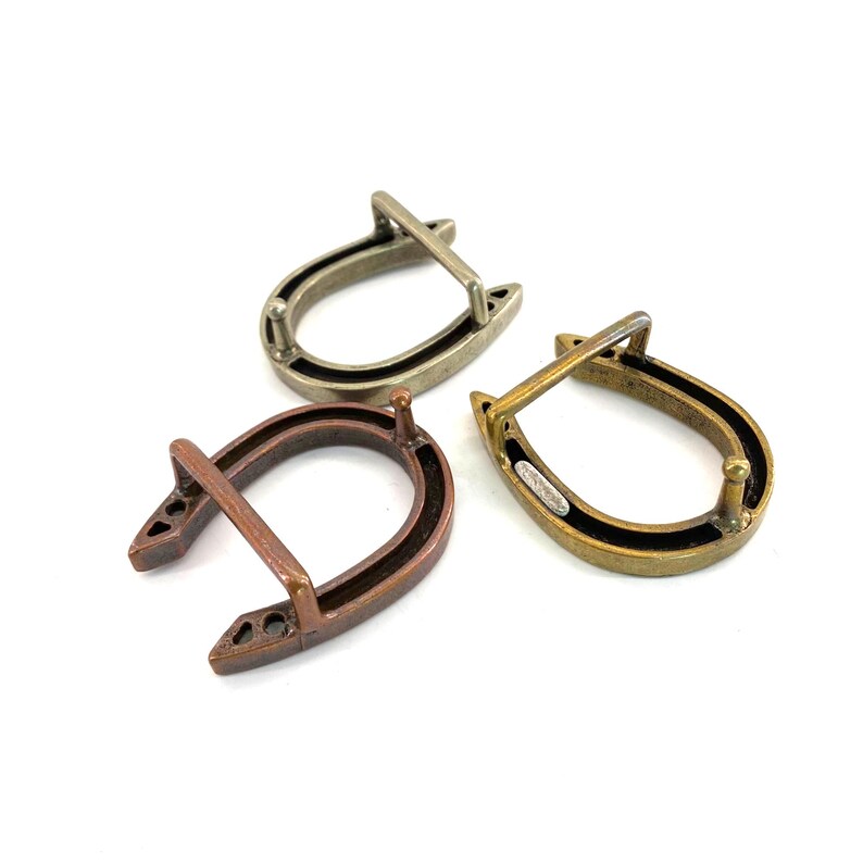 K&ouml;nnte beinhalten: Drei hufeisenf&ouml;rmige Metallschnallen in Bronze-, Silber- und Goldt&ouml;nen. Jede Schnalle hat eine schwarze Innenseite und einen Steg oben. Die Schnallen sind f&uuml;r Lederarbeiten oder andere Bastelprojekte konzipiert.