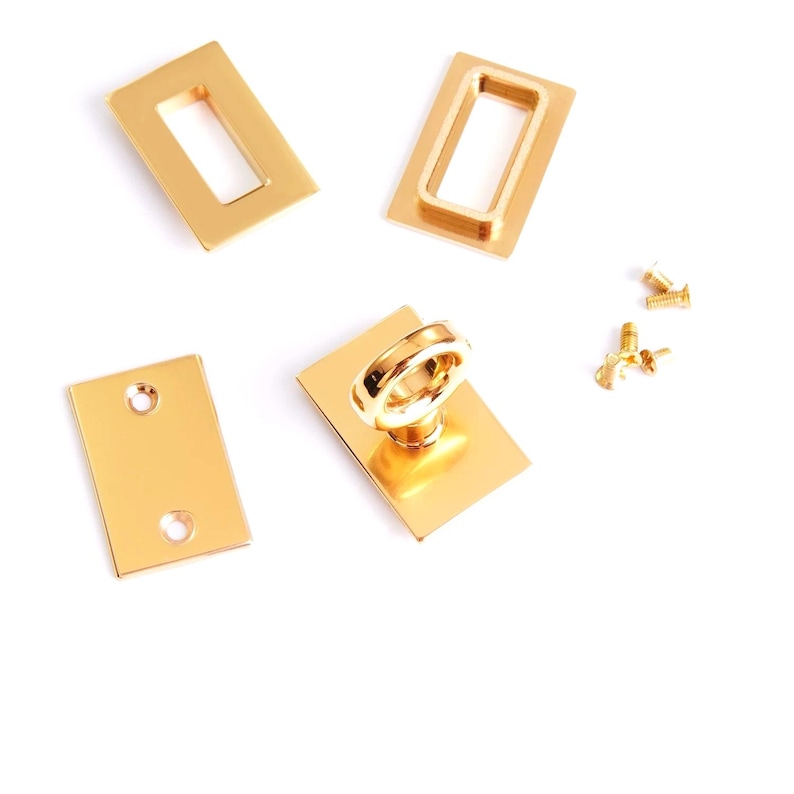 Pu&ograve; includere: Componenti hardware in metallo dorato, tra cui piastre rettangolari, telai e un anello di trazione, sono disposti su sfondo bianco. Sono presenti anche piccole viti. L'hardware &egrave; probabilmente per borse o altri accessori.