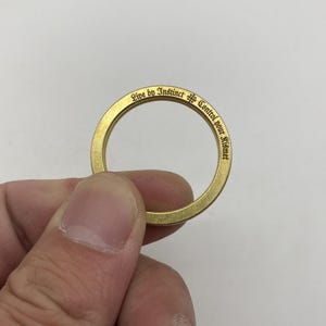 Op de afbeelding: Een gouden metalen ring met de inscriptie "Live by Instinct & Control your Kismet" in gotische letter.
