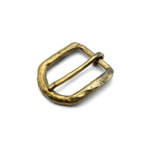 Può includere: Una fibbia in ottone con finitura martellata. La fibbia è rettangolare con angoli arrotondati e ha una finitura liscia e lucida.