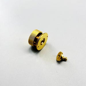 Pode incluir: Um conjunto de dois fechos magnéticos dourados. Uma parte é um disco redondo com um pequeno pino, e a outra é um cilindro maior e canelado preso a um disco plano. O hardware foi projetado para uso em bolsas ou outros projetos de artesanato.