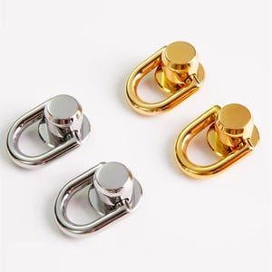 Op de afbeelding: Vier metalen D-ringconnectoren. Twee zijn zilverkleurig en twee goudkleurig. Elke connector heeft een cirkelvormige basis met een paal en een D-vormige ring. De connectoren staan op een witte achtergrond.
