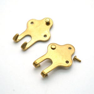 May include: Two brass-colored key-shaped hooks with a curved hook at the bottom and a small knob at the top. Each hook has three small holes. A small screw is also included.