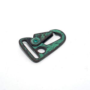 May include: A metal swivel clasp with a weathered, distressed appearance. The clasp is primarily green with areas of brown, showing signs of age and use. The design includes a rectangular loop and a spring-loaded hook.