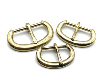 May include: Three gold-toned metal belt buckles of different sizes. The buckles are oval-shaped with a centre bar.