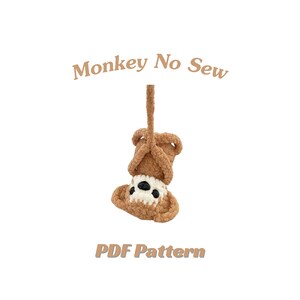 Puede incluir: Un mono de ganchillo hecho a mano, al revés, en tonos marrón, blanco y negro. El mono está suspendido por un cordón marrón. El texto de la imagen dice "Monkey No Sew" y "PDF Pattern".