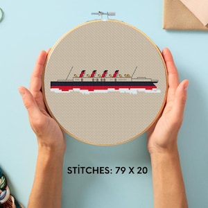 May include: Cross-stitch embroidery hoop with a red, black, and white ship design. The ship has multiple smokestacks and is set against a beige background. The text "STITCHES: 79 X 20" is visible at the bottom.