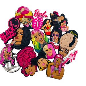 以下が含まれることがあります： 女性有名人の様々な漫画の肖像画が特徴の、カラフルな靴チャームのコレクション。 チャームはピンク、イエロー、ブラック、ブラウンの色合いで、「Barbz」、「Black Barbie」、「Icon」と書かれています。