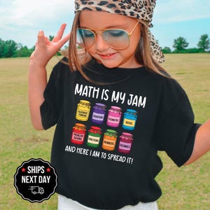 May include: Black t-shirt with the text "MATH IS MY JAM" and colorful jars labeled with math terms like "Algebraic Thinking" and "Fractions." The shirt also says "AND HERE I AM TO SPREAD IT!"