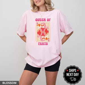 A woman wearing a pink t-shirt with a graphic design of a queen of ears and the text "QUEEN OF EARS" printed on it.