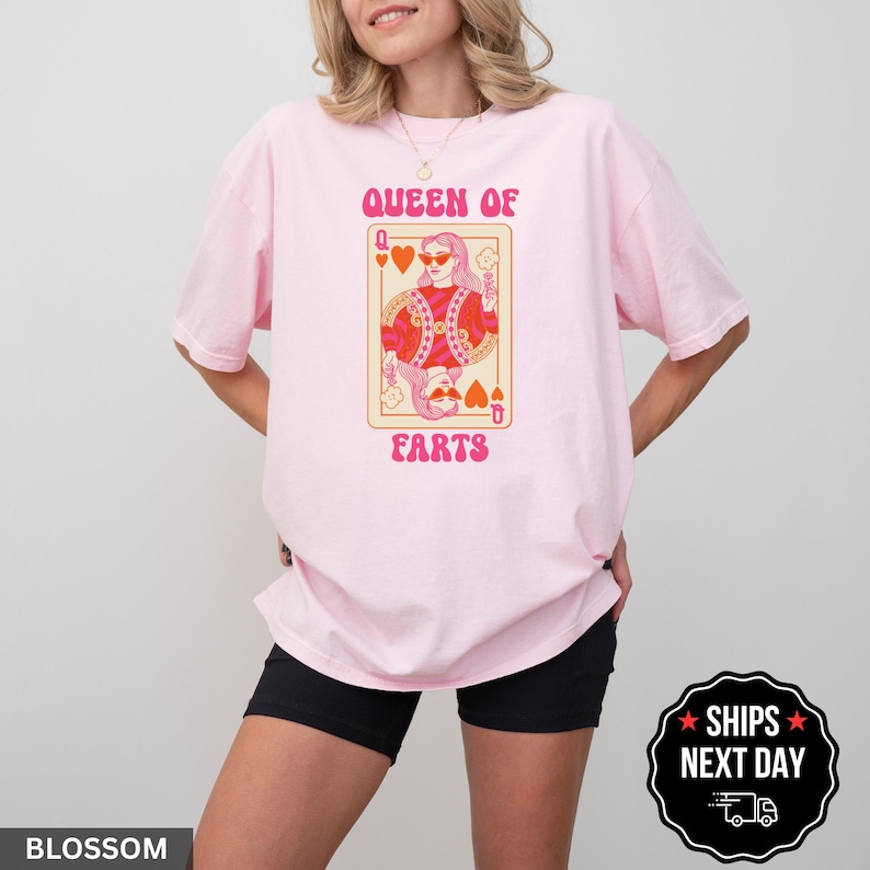 A woman wearing a pink t-shirt with a graphic design of a queen of ears and the text "QUEEN OF EARS" printed on it.