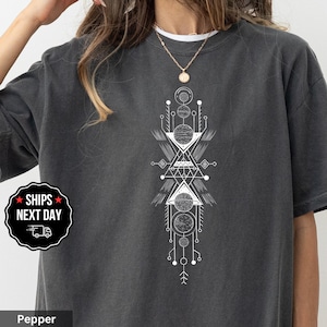 May include: Dark gray t-shirt with a white geometric design. The design features circles, triangles, and lines arranged in a vertical pattern. The shirt has a crew neck and short sleeves. The text "Pepper" is at the bottom of the image.