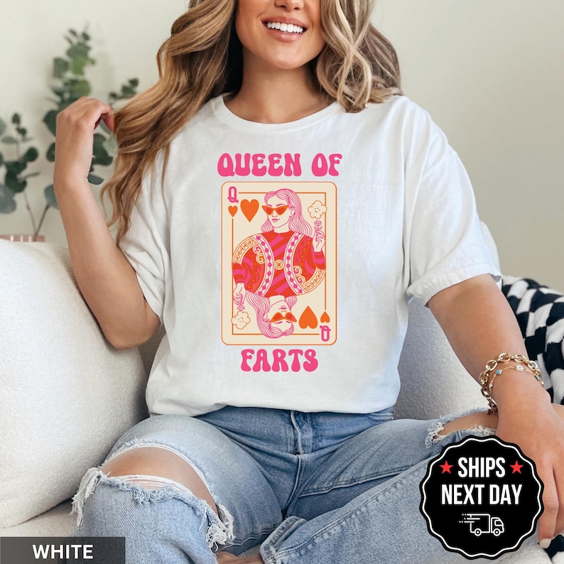 A woman wearing a white t-shirt with a graphic design of a woman holding a deck of playing cards and the text "Queen of Ears" printed on it.