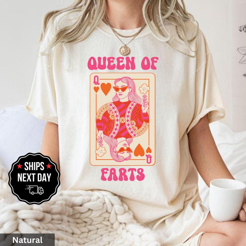 A woman wearing a white t-shirt with a graphic design of a woman's face and the text "Queen of Farts" printed on it.