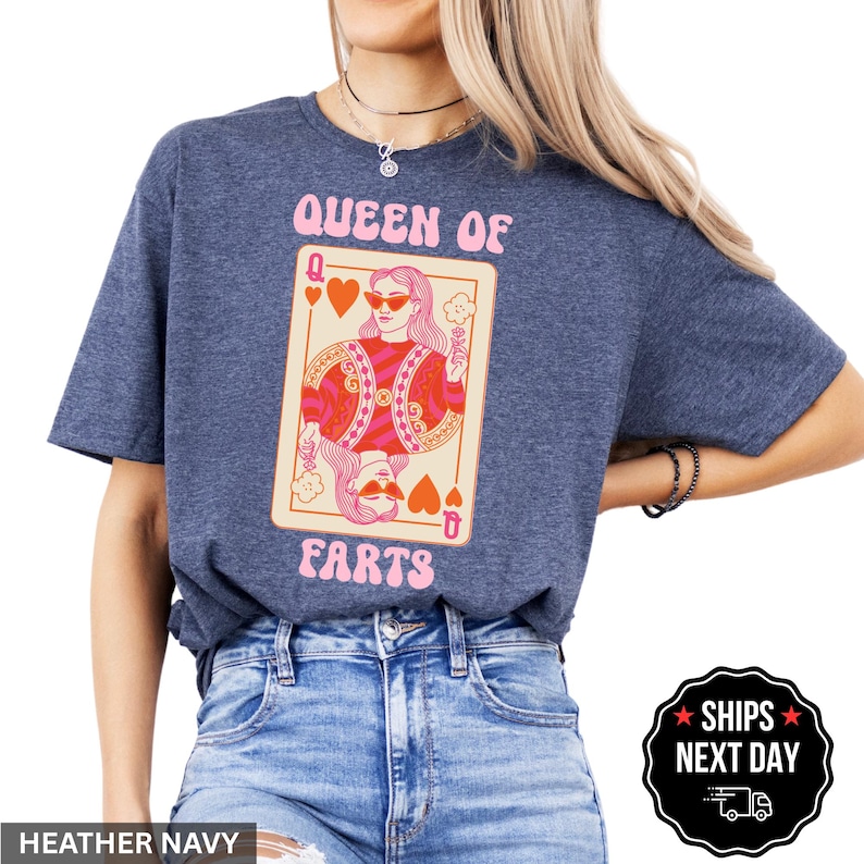 A woman wearing a blue t-shirt with a graphic design of a woman holding a deck of cards and the text "Queen of Farts" printed on it.
