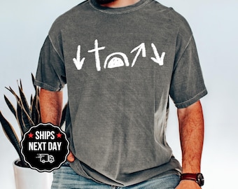 May include: A gray t-shirt with a white graphic featuring a cross, arrows, and a semi-circle. The shirt is a muted gray color and has a slightly worn appearance. The text on the shirt appears to be hand-drawn.