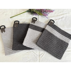 May include: Four crocheted pot holders in shades of gray and white are displayed. Each square holder has a loop for hanging and a small tag that reads "Made with Love." The pot holders are arranged on a white surface, with a sprig of lavender in the background.