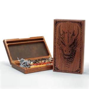 May include: A wooden dice box with an open lid, revealing dice and miniature figurines. The box is made of dark wood and has a brass hinge. A separate wooden panel with a dragon's head etched on it is also visible.