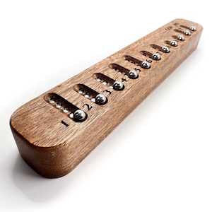 May include: A wooden counting tool with a series of oval cutouts, each containing a small, silver ball. Numbers 1 through 9 are etched along the top. The tool is made of light brown wood and has a smooth, polished finish.