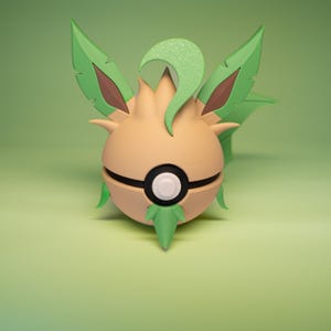 Könnte beinhalten: Ein 3D-gedrucktes Modell eines Pokémon-Charakters, ein hellbraunes Evoli mit grünen, blattförmigen Anhängseln und einem Pokeball-Design auf seinem Körper.
