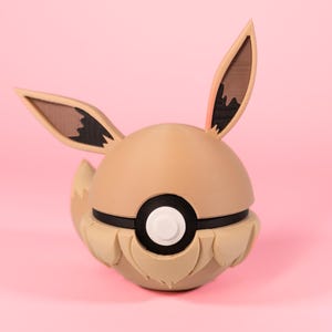 Könnte beinhalten: Eine braune und schwarze Eevee-Pokémon-Figur mit einem Pokeball-Design. Die Figur hat große Ohren und einen flauschigen Schwanz.