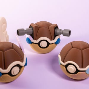 Könnte beinhalten: Drei braune und blaue Spielzeug-Schildkrötenfiguren. Eine Schildkröte hat weiße Flügel, eine hat graue Kanonen und eine hat blaue Flügel.