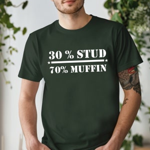 May include: Dark green t-shirt with the text "30 % STUD / 70% MUFFIN" in white block letters. The text is centered on the chest, with a line separating the two phrases. The shirt is a crew neck style.