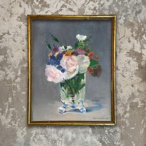 May include: An oil painting of a floral arrangement in a clear glass vase with a gold frame. The bouquet features pink, white, and purple flowers with green foliage. The vase sits on a light blue surface against a gray background.