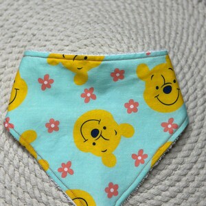 May include: A light blue baby bib with a Winnie the Pooh design. The bib features a repeating pattern of Winnie the Pooh's face and pink flowers.