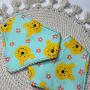 May include: Two turquoise blue baby bibs with a yellow Winnie the Pooh character and pink flower pattern.