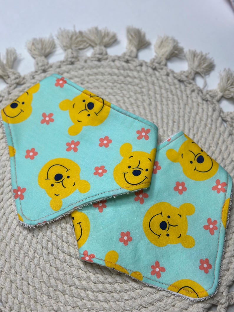 May include: Two turquoise blue baby bibs with a yellow Winnie the Pooh character and pink flower pattern.
