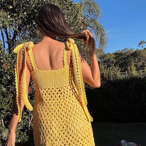 Peut inclure: Une robe jaune en crochet avec des bretelles nou&eacute;es. La robe pr&eacute;sente une encolure carr&eacute;e et un motif ajour&eacute; textur&eacute;. Les bretelles sont nou&eacute;es aux &eacute;paules. La robe est de couleur jaune vif.