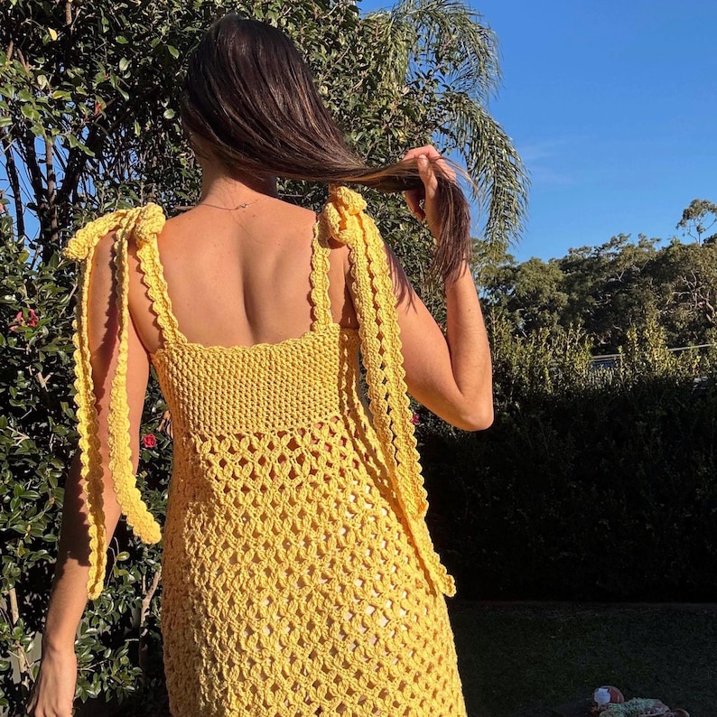 Peut inclure: Une robe jaune en crochet avec des bretelles nou&eacute;es. La robe pr&eacute;sente une encolure carr&eacute;e et un motif ajour&eacute; textur&eacute;. Les bretelles sont nou&eacute;es aux &eacute;paules. La robe est de couleur jaune vif.