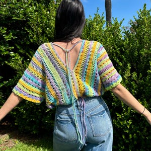 Peut inclure: Un haut en crochet coloré avec un laçage dans le dos. Le haut est fait de plusieurs couleurs, dont le jaune, le vert, le bleu et le violet. Le haut est court et ample.