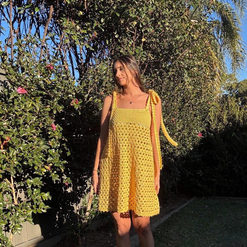 Peut inclure: Robe jaune au crochet avec encolure carr&eacute;e et bretelles nou&eacute;es. La robe arrive au genou et pr&eacute;sente un motif ajour&eacute; ample. La robe est faite d'un fil jaune vif et convient aux temp&eacute;ratures chaudes.