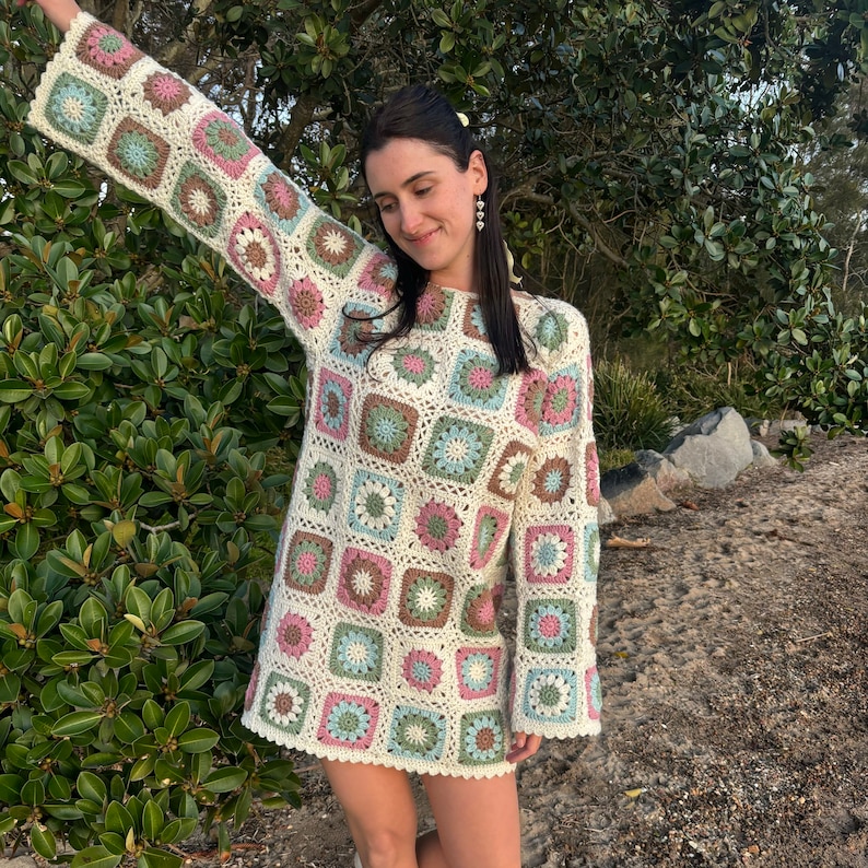 Girl wearing flower granny square crochet dress with left arm in the air smiling.